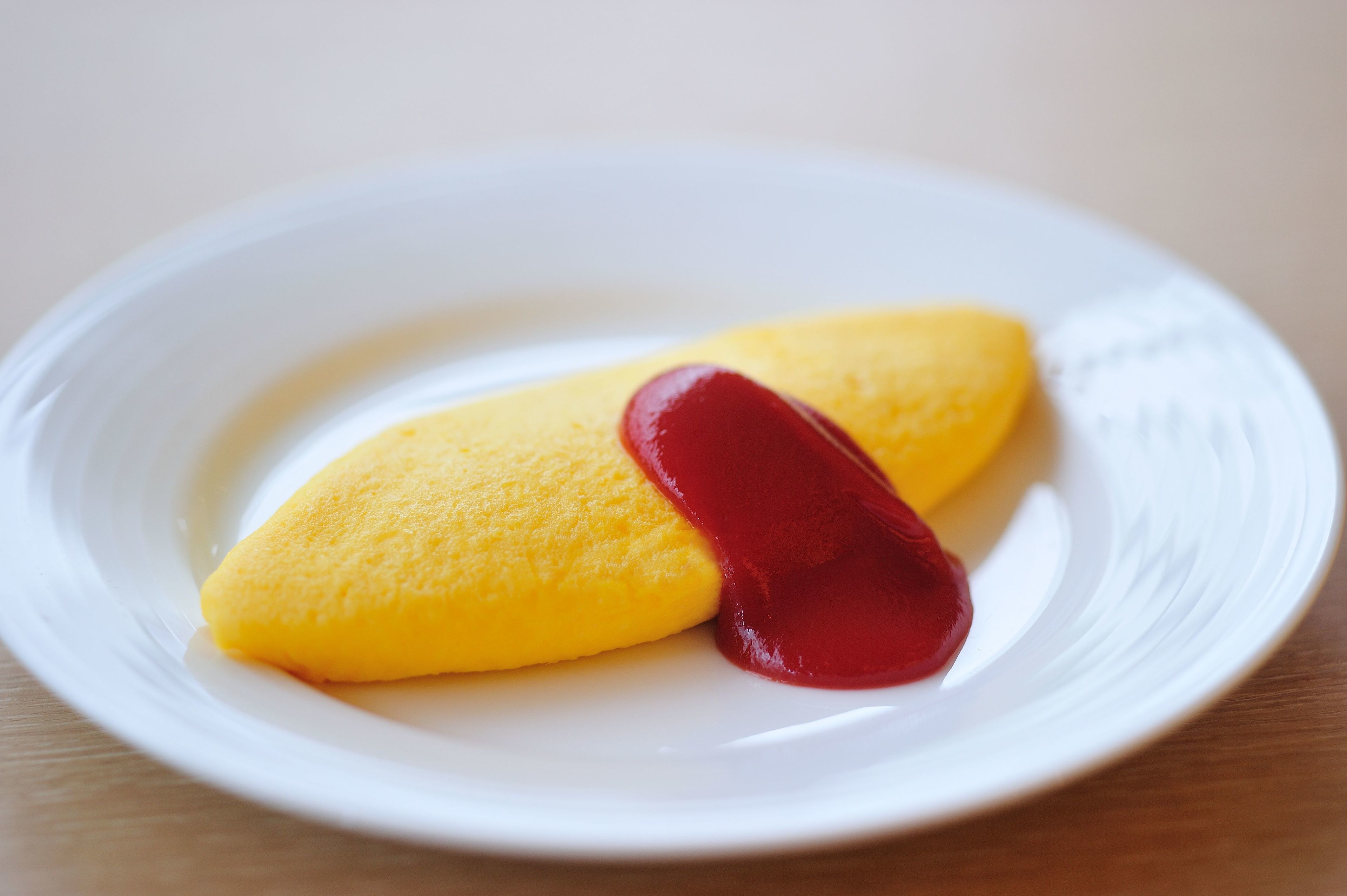 A white plate with two yellow items and a red item on a wooden surface.