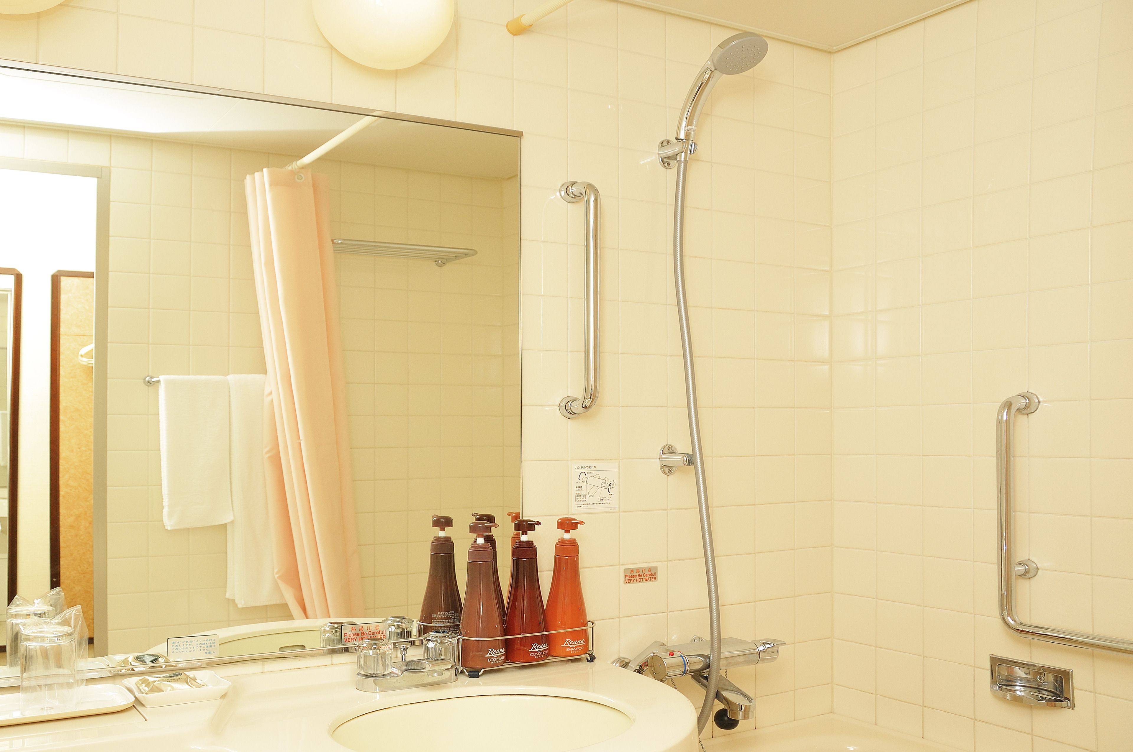 A bathroom with a sink, mirror, shower, and handrails.