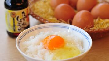 A bowl of white rice with an egg yolk in the center, a bottle with a label, and a basket with eggs in the background.