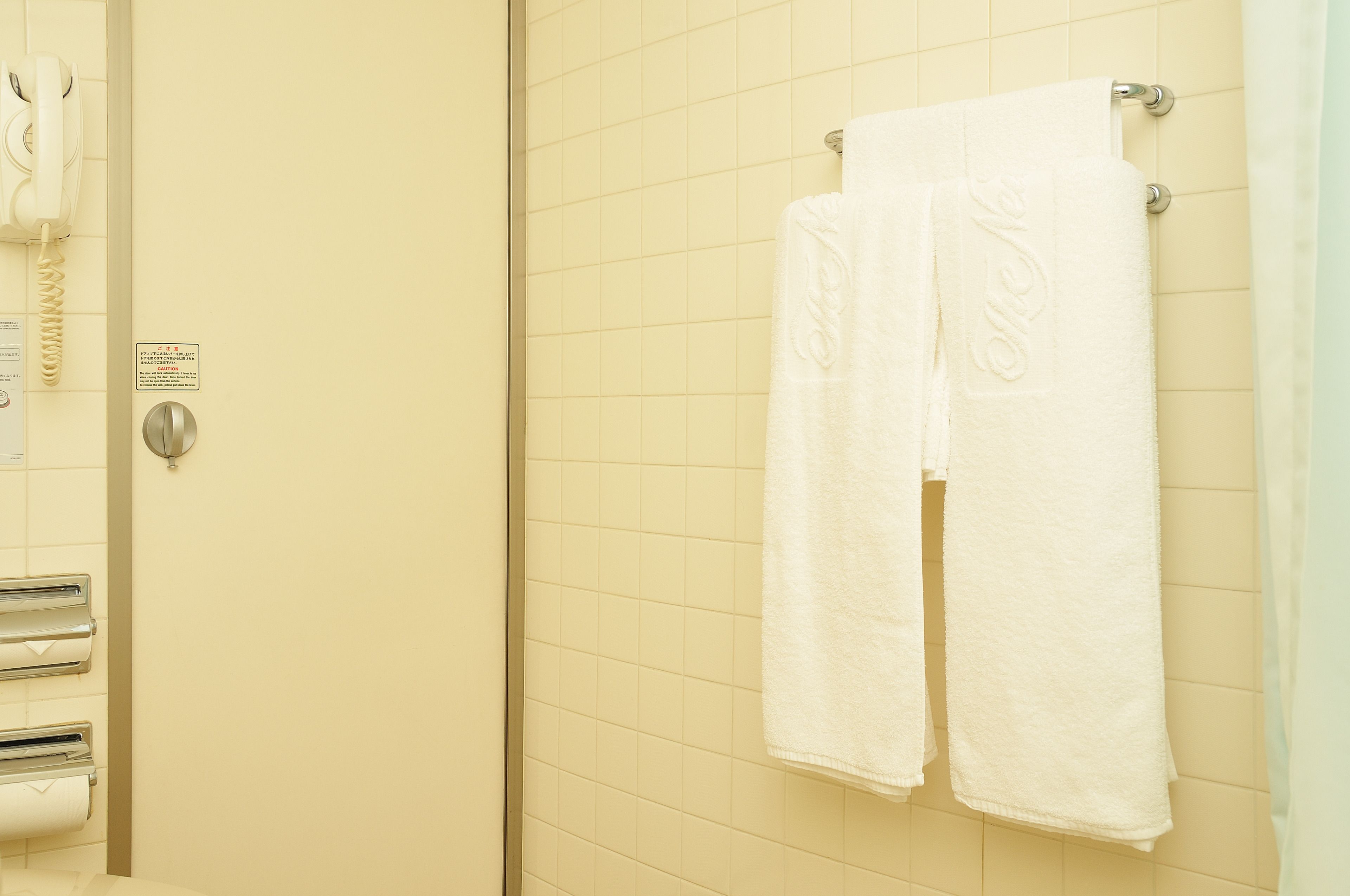 Ein Badezimmer mit einem weißen Handtuch an einem Haken, einem Handtrockner und einem Toilettenpapierhalter.