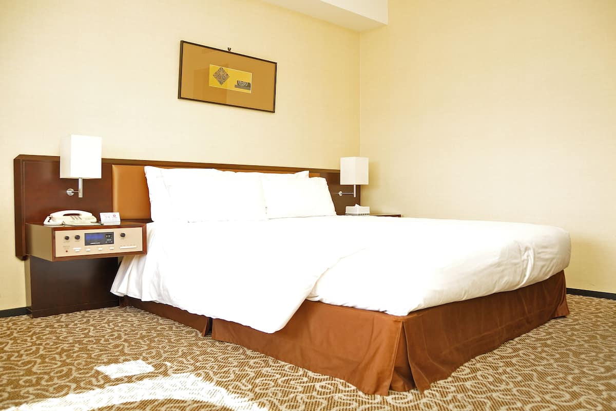 Ein Hotelzimmer mit einem großen Bett, zwei Nachttischen, einem fest montierten Telefon und einem gerahmten Bild über dem Bett.