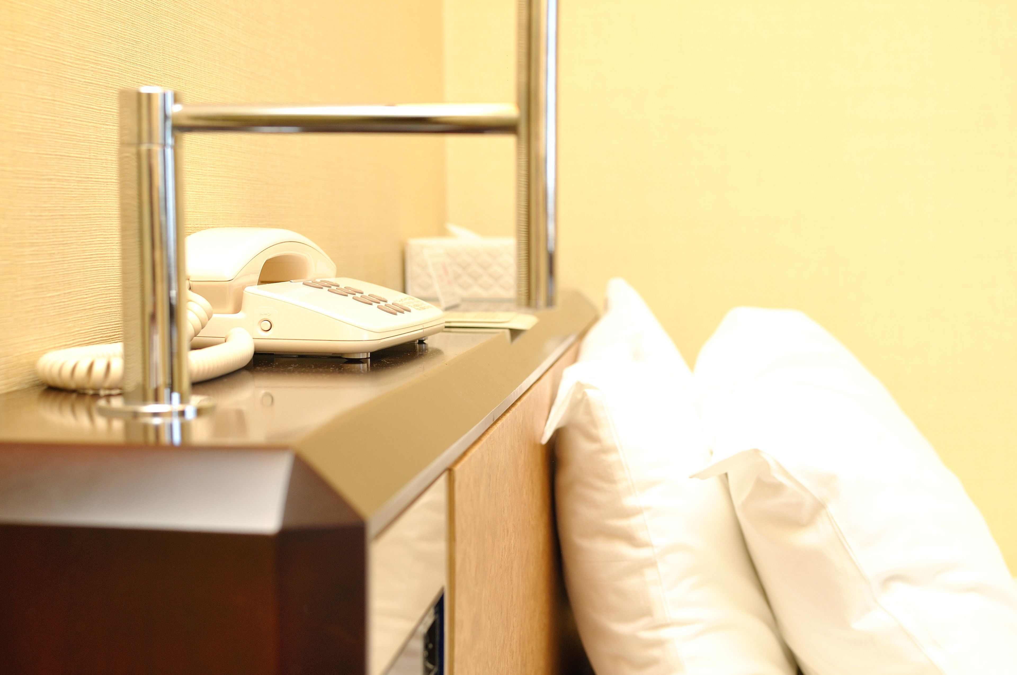 A hotel room with a bedside telephone, a tissue box, and a white pillow on the bed.