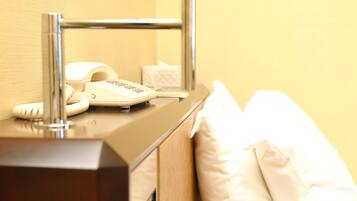 A hotel room with a bedside telephone, a tissue box, and a white pillow on the bed.