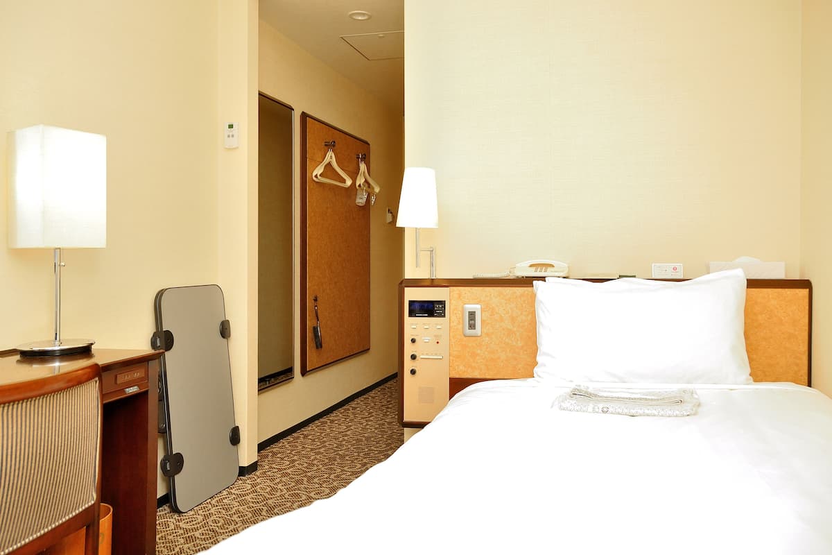 Ein Hotelzimmer mit Bett, Schreibtisch, Lampe, Telefon und Kleiderhaken.