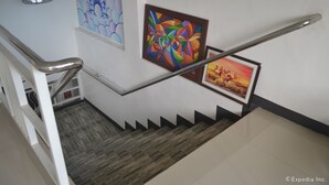 A staircase with a metal handrail, wooden steps, and three framed artworks on the walls. - Pearl Suites (General Santos)