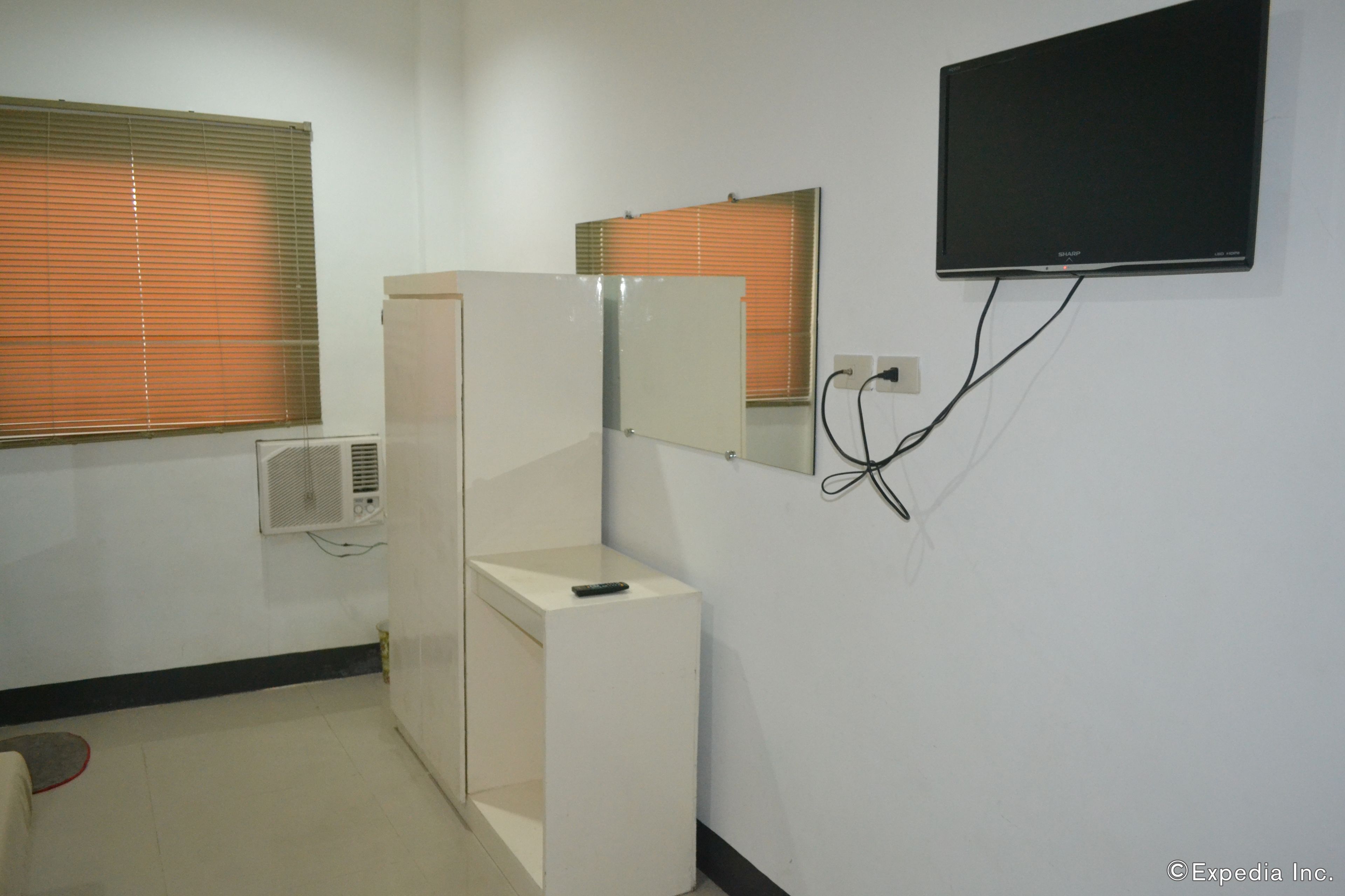 A hotel room with a bed, a bedside table, a mirror, a TV mounted on the wall, and a window with blinds.