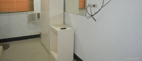 A hotel room with a bed, a bedside table, a mirror, a TV mounted on the wall, and a window with blinds.