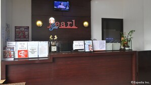 A hotel reception desk with a neon sign reading "Pearl", a television mounted on the wall, and various informational signs including Wi-Fi, Xerox, and a pay-as-you-check-in option. - Pearl Suites (General Santos)