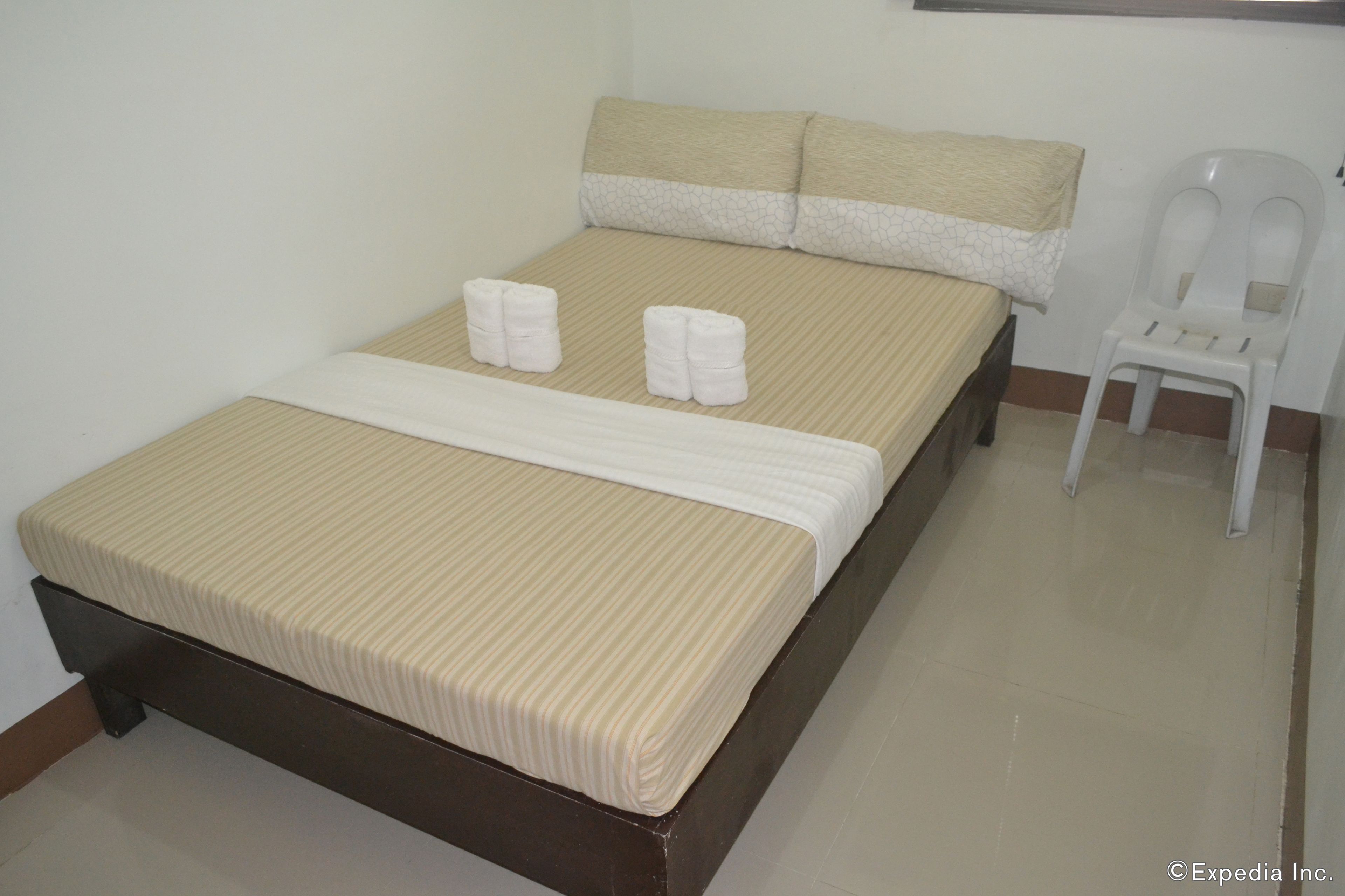 A neatly made bed with a striped bedspread and two rolled towels on the side.