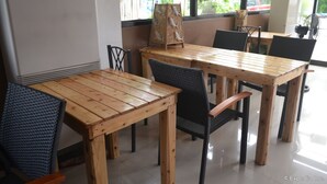 A restaurant interior with wooden tables and chairs, a large window with a view of the outside, and a fan near the window. - Pearl Suites (General Santos)
