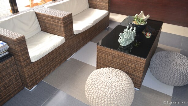 A wicker sofa with white cushions, a black coffee table with decorative items, and two round poufs. - Pearl Suites (General Santos)