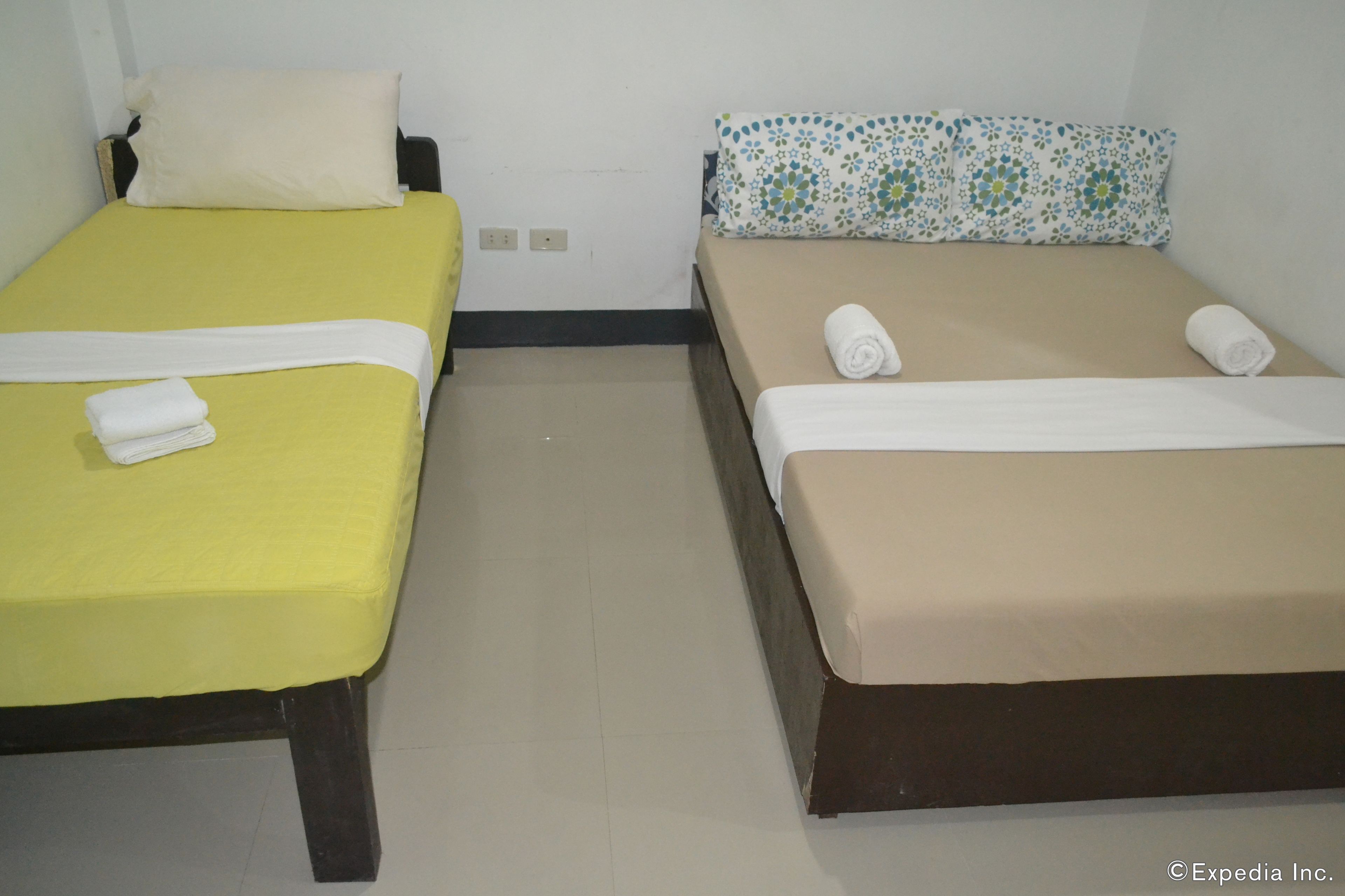Two single beds with white and beige bedding, a white pillow on the left bed, and a floral pillow on the right bed.