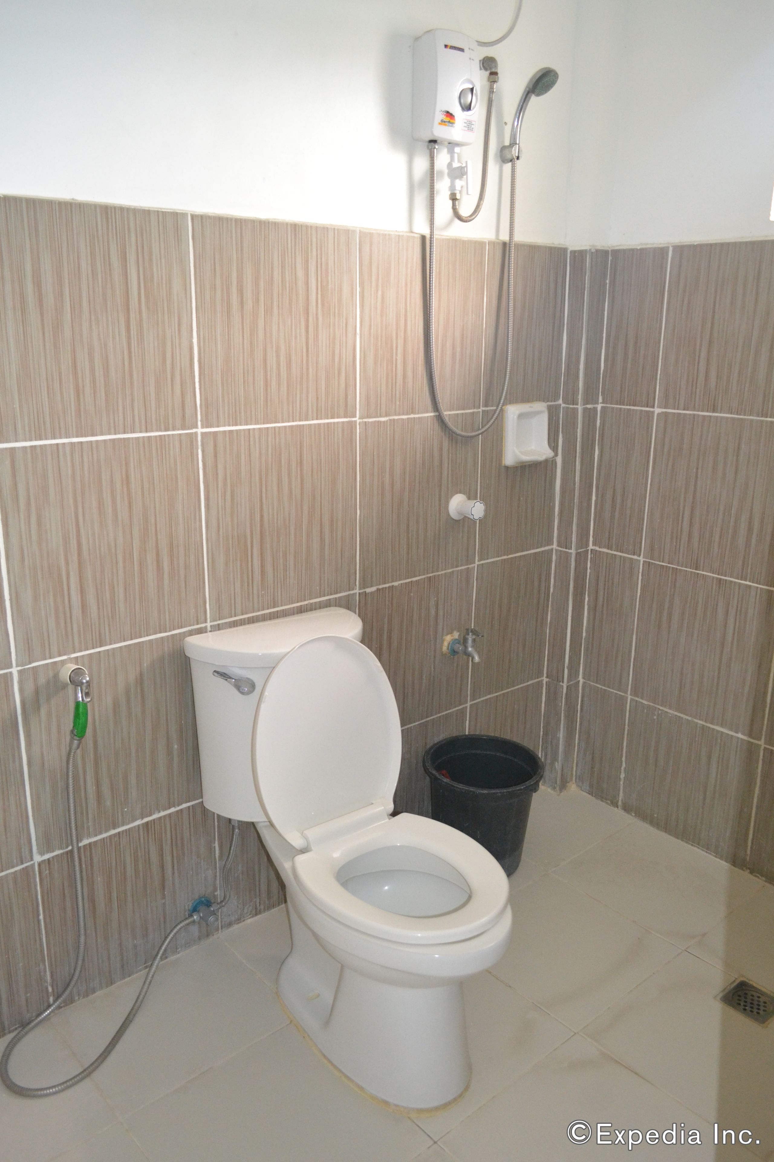 A bathroom with a toilet, a shower unit, and a black trash bin.