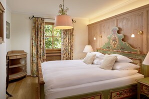 A bedroom with a wooden headboard, a bed with white linens, a nightstand, a lamp, and a window with curtains.