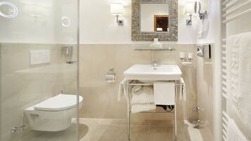 A modern bathroom with a glass shower enclosure, a white toilet, a glass-topped sink, and a mirror with decorative framing.