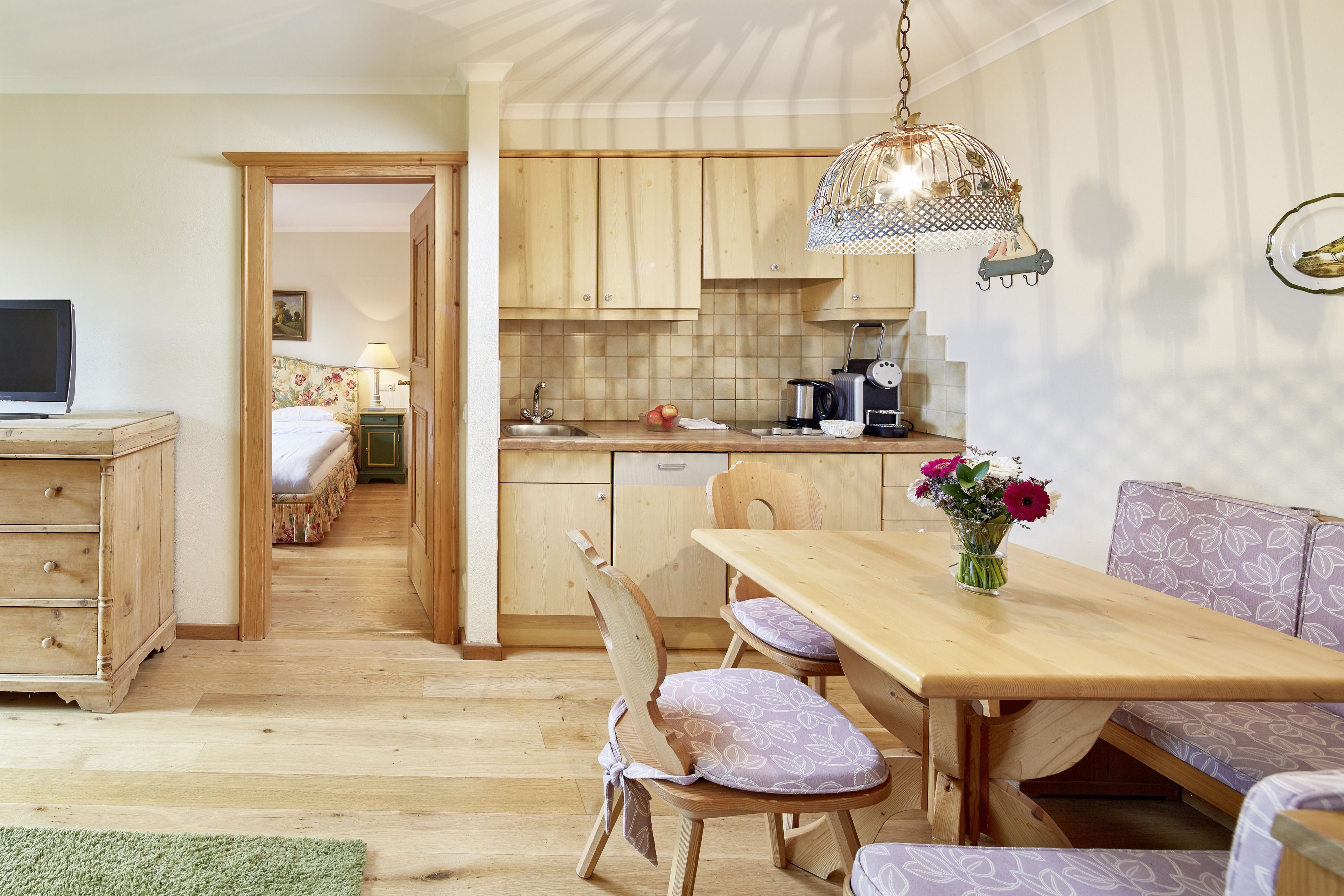 A cozy room with a wooden dining table, a sofa, and a kitchen area with wooden cabinets and a hanging light fixture.