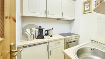 A kitchen with white cabinets, a stainless steel sink, a stove, and a coffee maker.