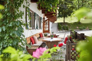 An outdoor seating area with wooden benches and tables, surrounded by lush greenery and flowers.
