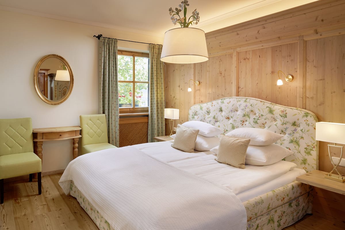 A bedroom with a large bed, two bedside tables, a mirror, and a window with curtains.