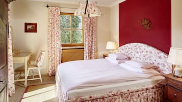 A bedroom with a bed, a desk, a chair, a window with curtains, and a lamp on a bedside table.