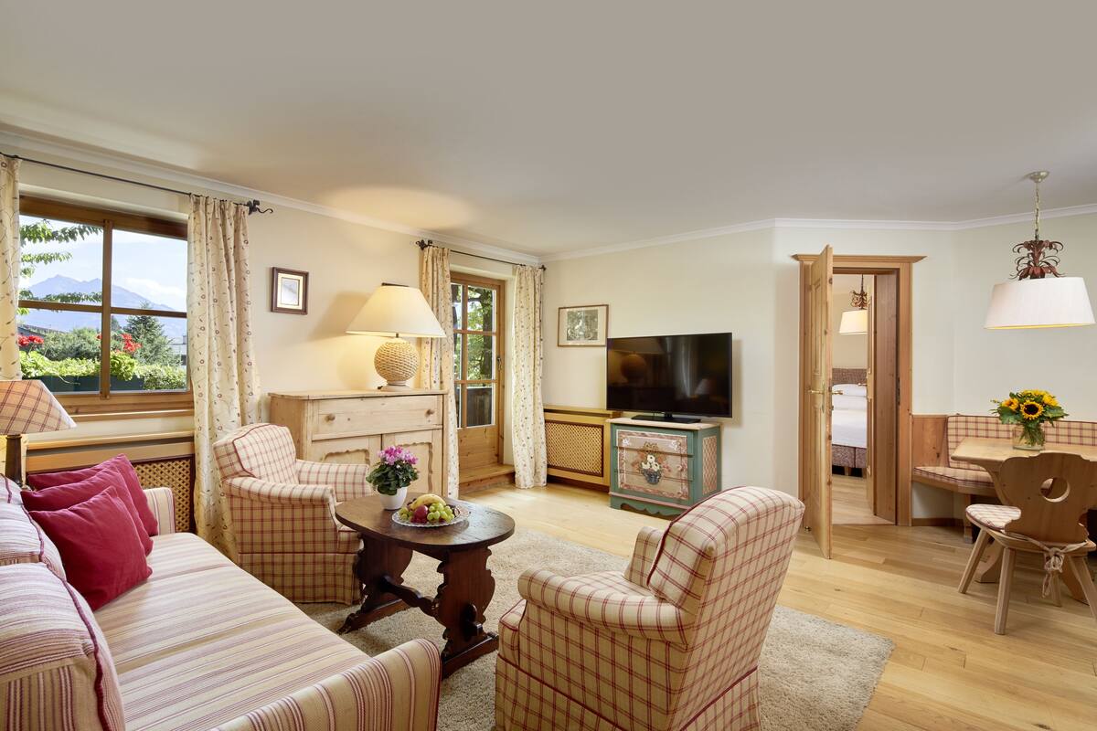 A cozy living room with a sofa, chairs, a TV, and a dining table with a vase of flowers.