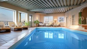 An indoor swimming pool with lounge chairs and a dining area. - Landsitz Römerhof - Hotel Apartments (Kitzbuhel)