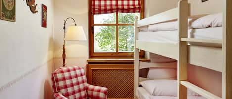 Ein kleiner, gemütlicher Raum mit einem Etagenbett, einem Stuhl, einem Tisch und einem Fenster mit kariertem Vorhang.