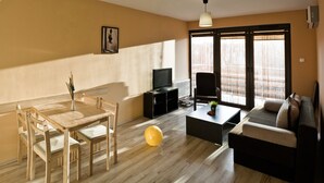 A living room with a wooden floor, a dining table with chairs, a sofa, a coffee table, a TV, and a window with blinds. - Baltic Sol (Wladyslawowo)