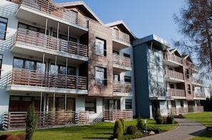 Um edifício residencial moderno, com várias andares, varandas, grandes janelas e um gramado bem cuidado.