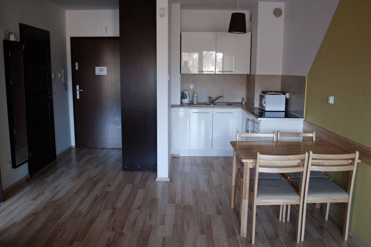 A modern kitchen with white cabinets, a wooden dining table with four chairs, and a microwave.