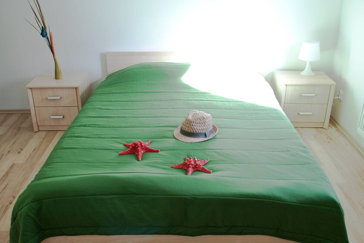 A neatly made bed with a green bedspread, two starfish decorations, and a straw hat on the bed.