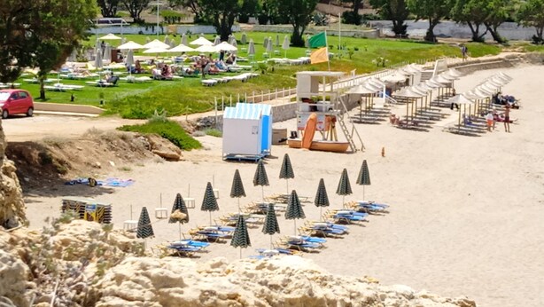 A beach with rows of umbrellas and lounge chairs, a lifeguard tower, and a grassy area with people. - Ilona Apartments (Chania)