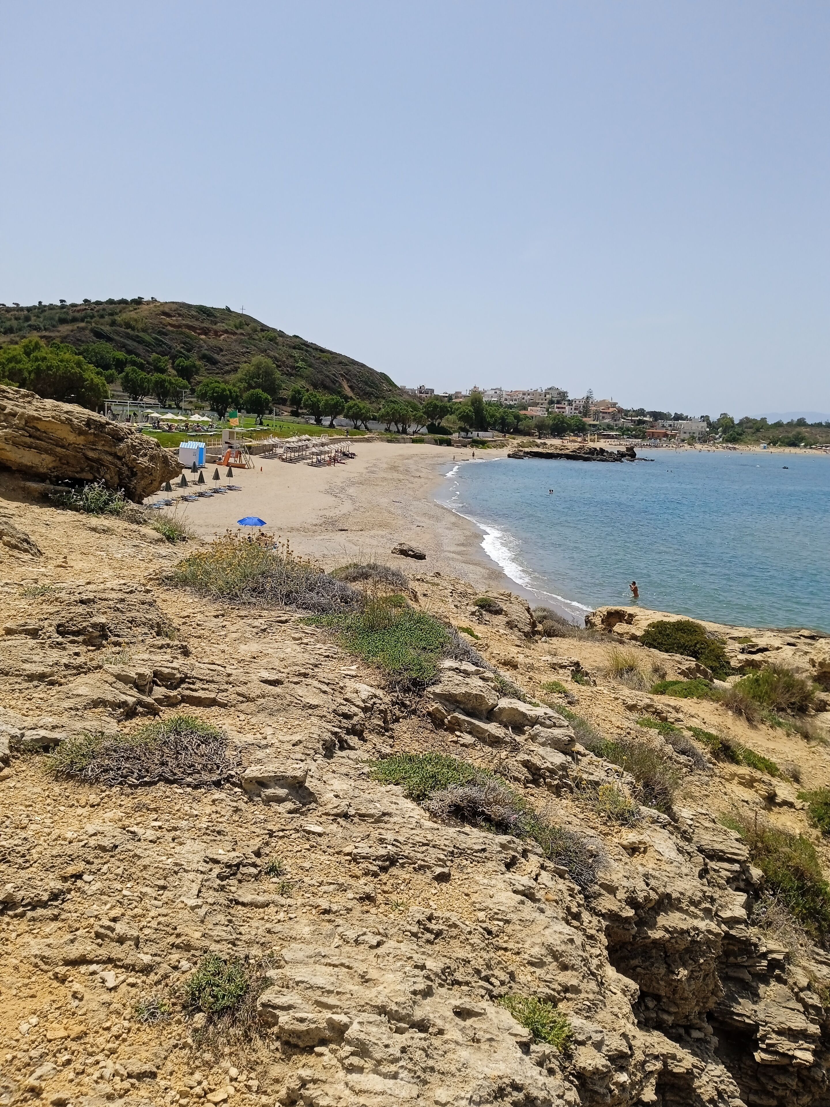 A coastal landscape with a sandy beach, rocky terrain, and a clear view of the sea.