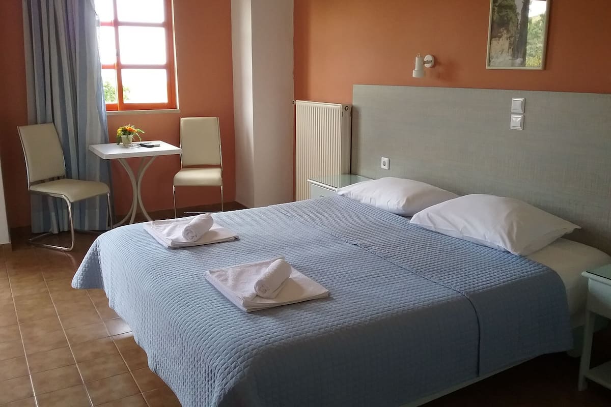 A hotel room with a bed, two chairs, a small table, and a window.