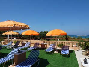 A rooftop terrace with striped lounge chairs and orange umbrellas, overlooking a scenic coastline. - Ilona Apartments (Chania)