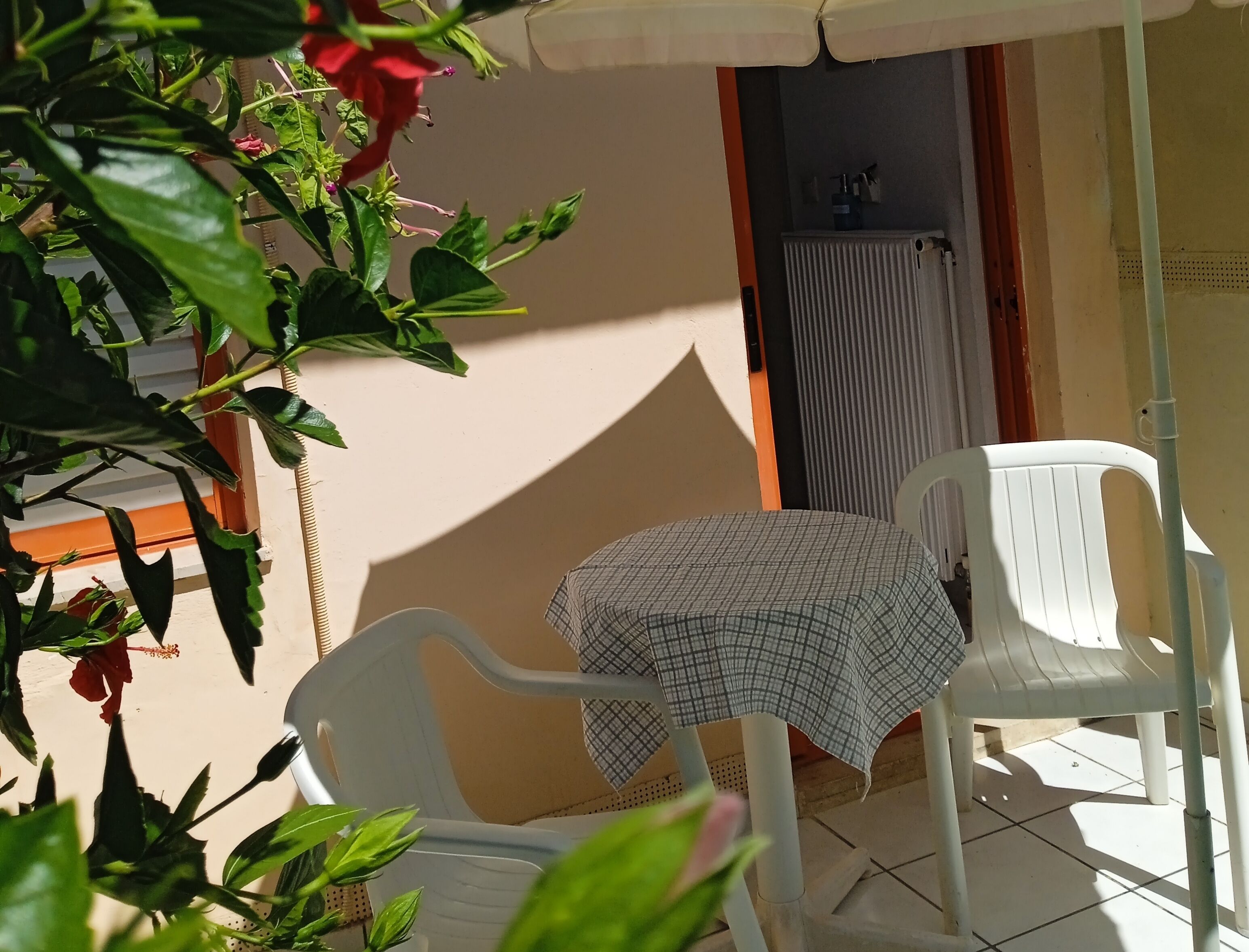 Un pequeño patio con dos sillas de plástico blanco y una mesa cubierta con mantel a cuadros.