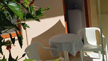 Un pequeño patio con dos sillas de plástico blanco y una mesa cubierta con mantel a cuadros.
