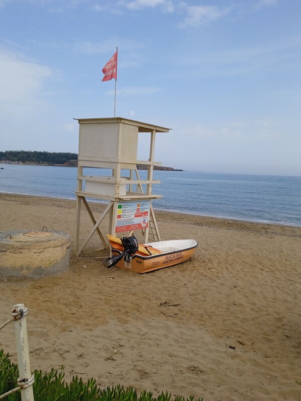 Una torre de salvavidas con una bandera, un bote de rescate y un cartel en una playa arenosa.