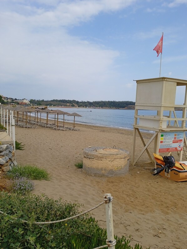 Una playa con una torre de salvavidas, sombrillas y sillas reclinables.