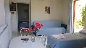 A room with a bed, a sofa, a table with a vase of flowers, and a window with curtains. - Ilona Apartments (Chania)