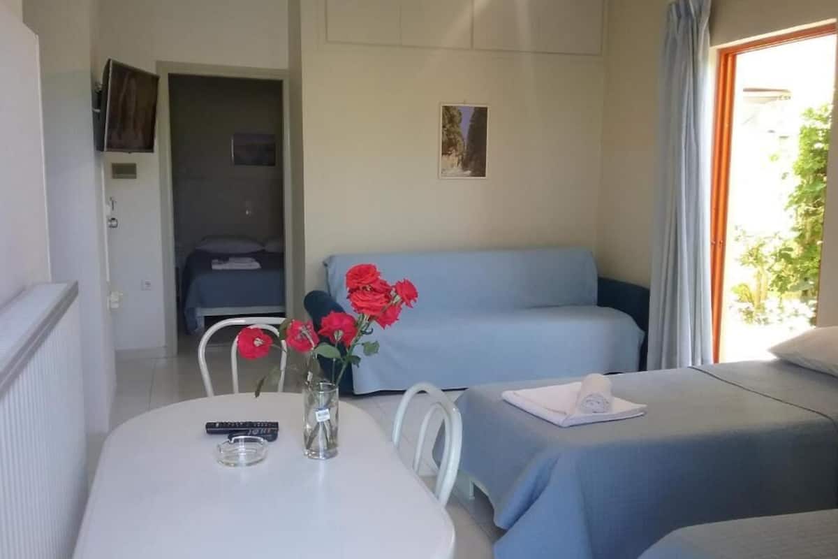 A room with a bed, a sofa, a table with a vase of flowers, and a window with curtains.