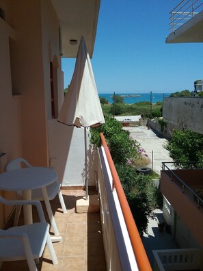 Un balcón con vista al mar, sillas de plástico blancas y una sombrilla blanca.