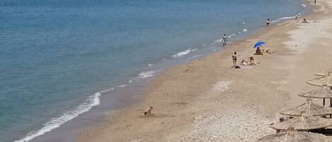 Une plage avec des galets, des parasols et des gens.