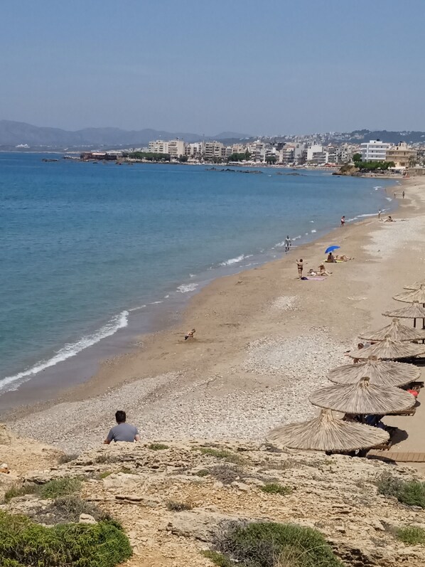Una playa con piedras, sombrillas y gente.