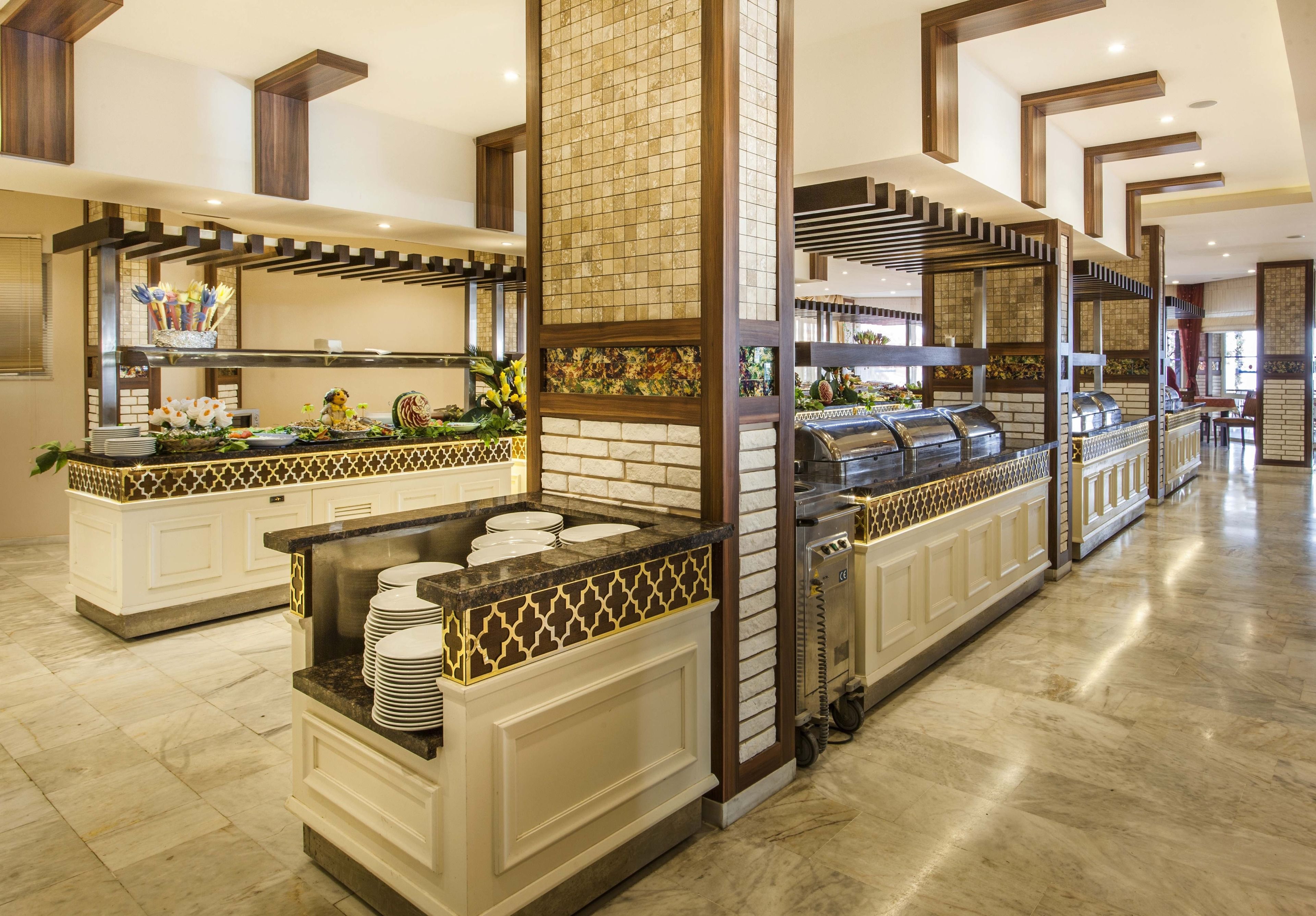 A hotel buffet area with multiple serving stations, a central pillar, and a tiled backsplash.