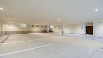 A spacious indoor parking area with multiple parking spaces, a row of bicycles, and a door leading to a hallway.