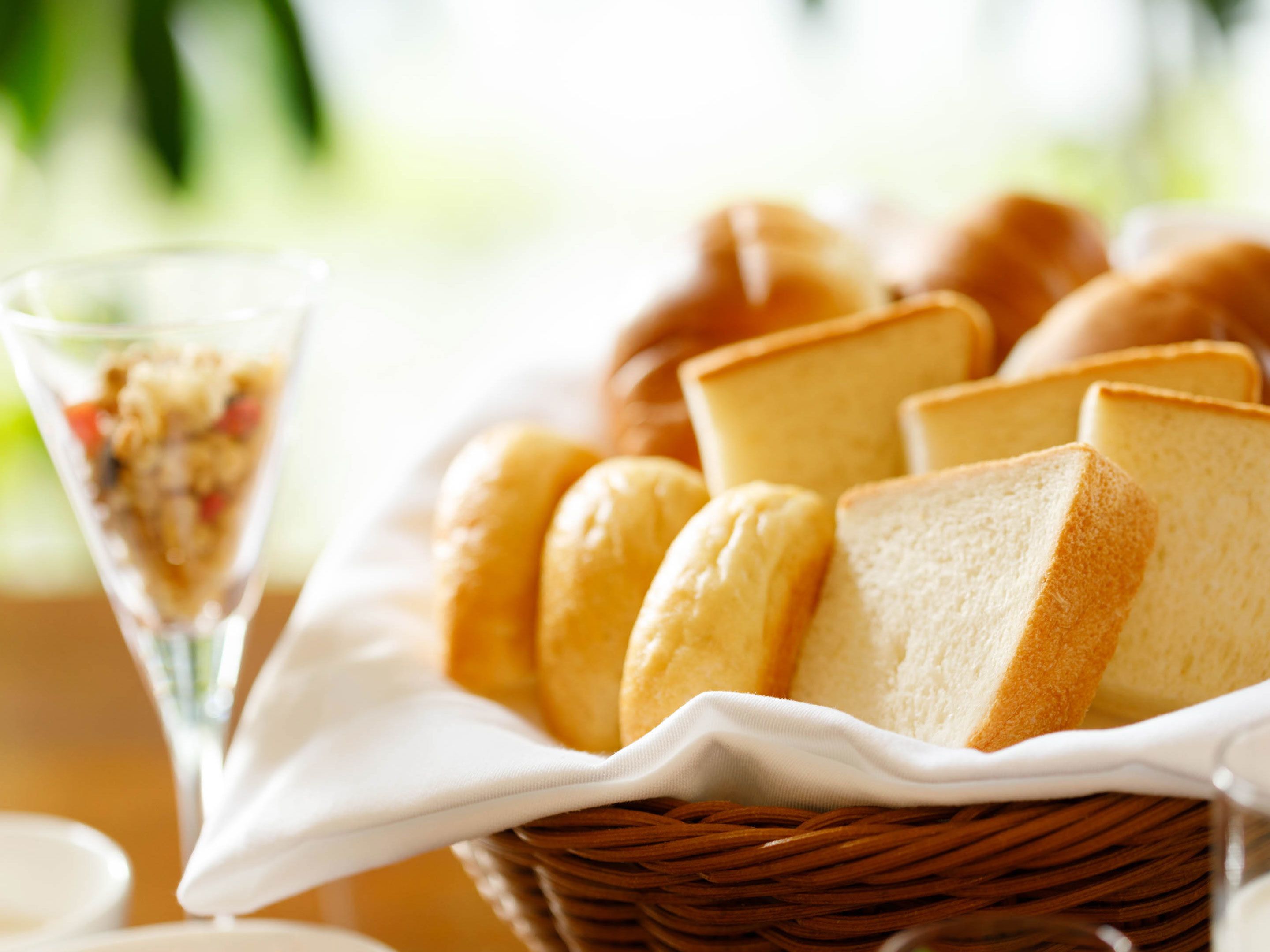 A basket of bread rolls and a glass of a layered dessert.