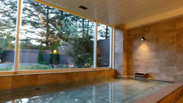 A modern indoor swimming pool with large windows, a stone wall, and a small seating area.