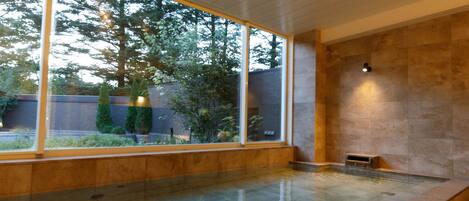 Una piscina interior moderna con ventanas amplias, una pared de piedra y una pequeña zona de estar.