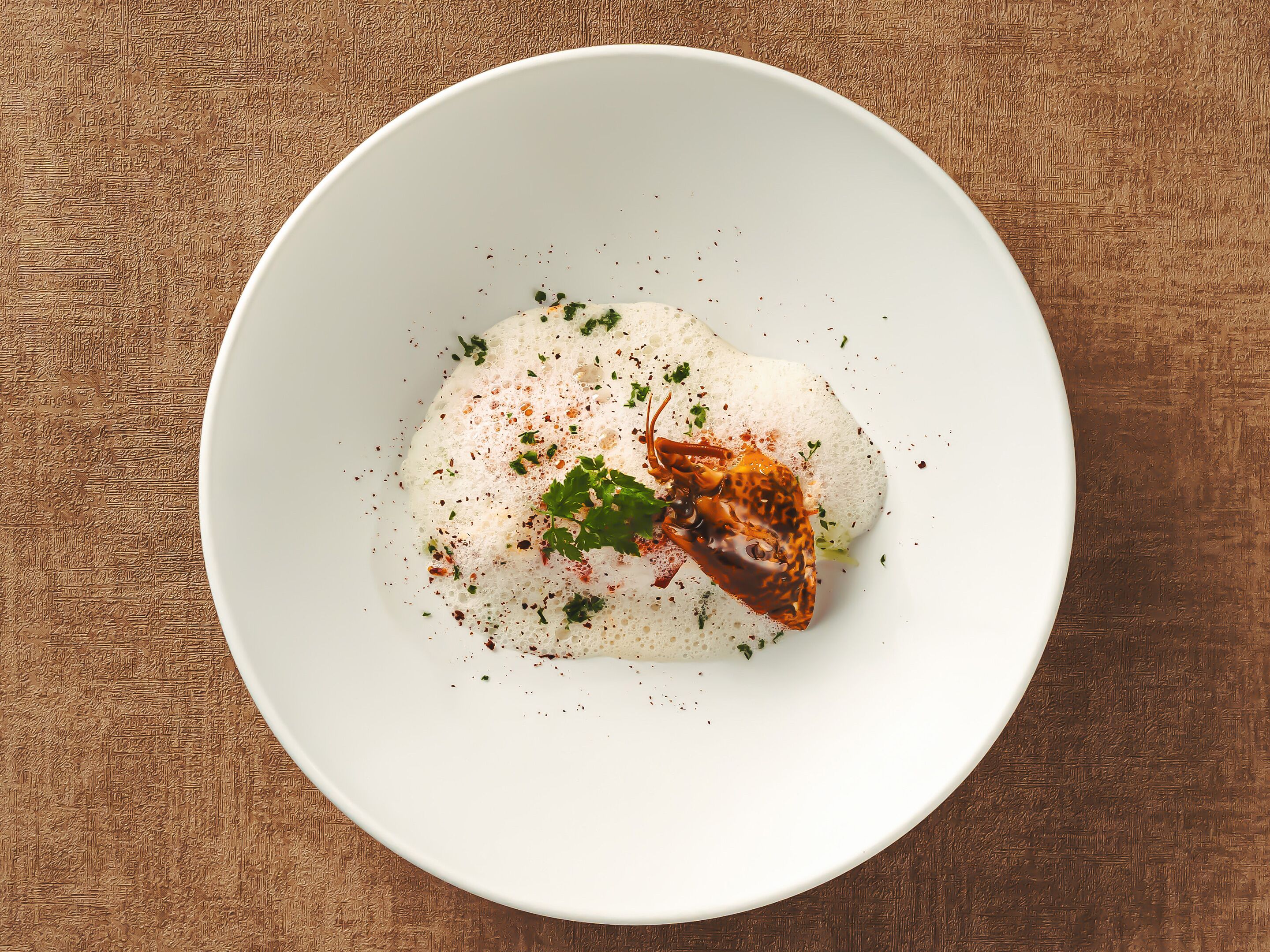 A white bowl with a white substance, garnished with herbs and spices, on a textured brown surface.